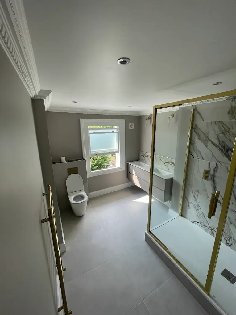 Brass-framed corner shower enclosure with marble tiling beside wall-hung vanity unit