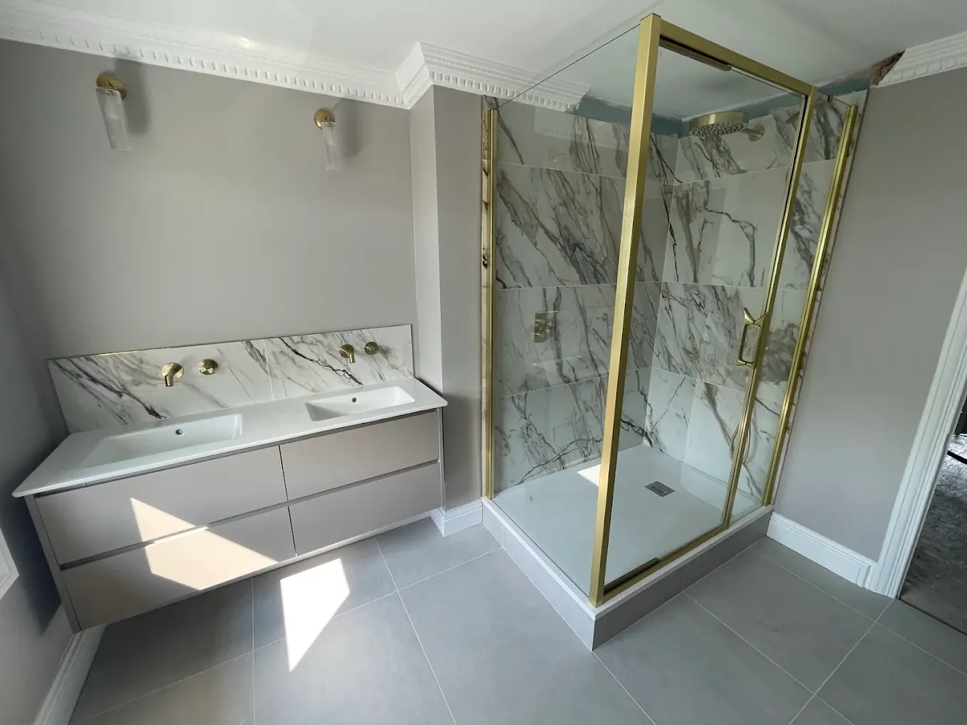 Wall-hung vanity with brass wall-mounted taps and marble splashback next to the shower enclosure