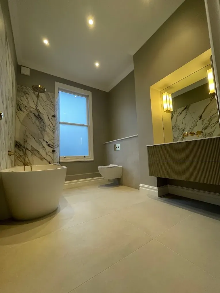 Full view of renovated bathroom with freestanding bath, wall-hung toilet and lit vanity mirror