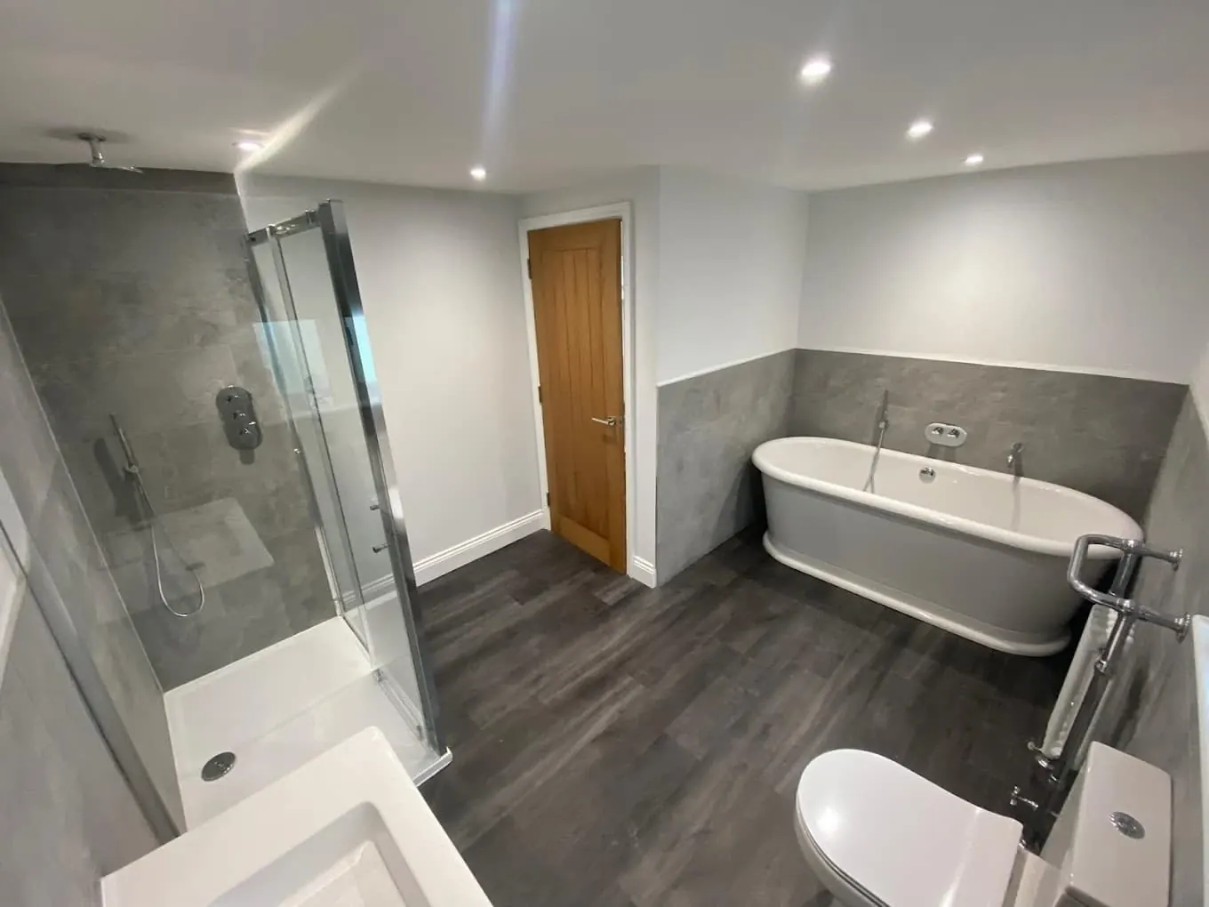 Grey freestanding roll-top bath with shower enclosure and wood-effect flooring