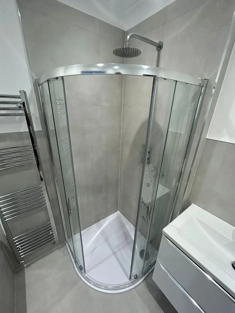 Quadrant sliding-door shower enclosure with rainfall head, grey tiling and chrome towel radiator