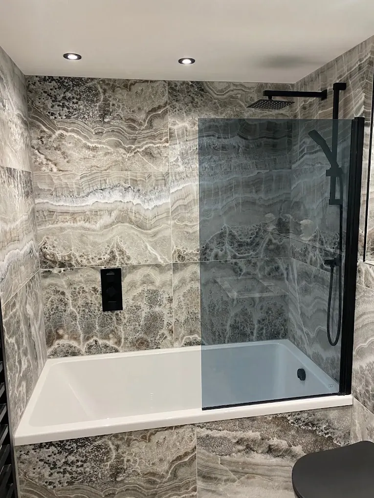 Bath with black-framed glass screen and black rainfall shower against stone-effect tiles