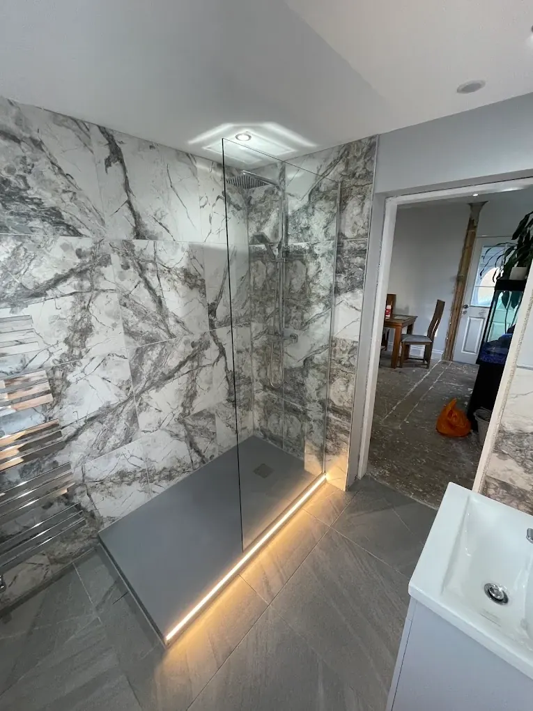 Walk-in glass shower with marble-effect wall panels and LED strip lighting along the tray