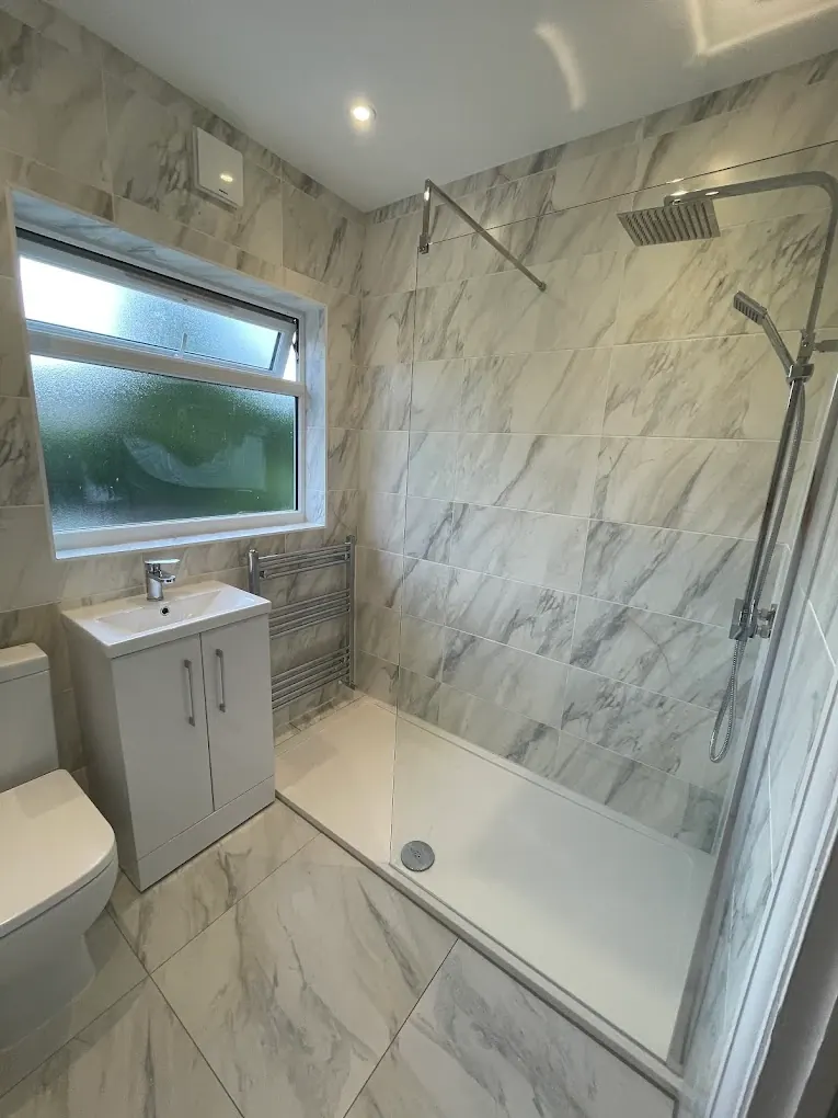 Walk-in shower with marble-effect tiles, chrome rainfall head and white vanity unit
