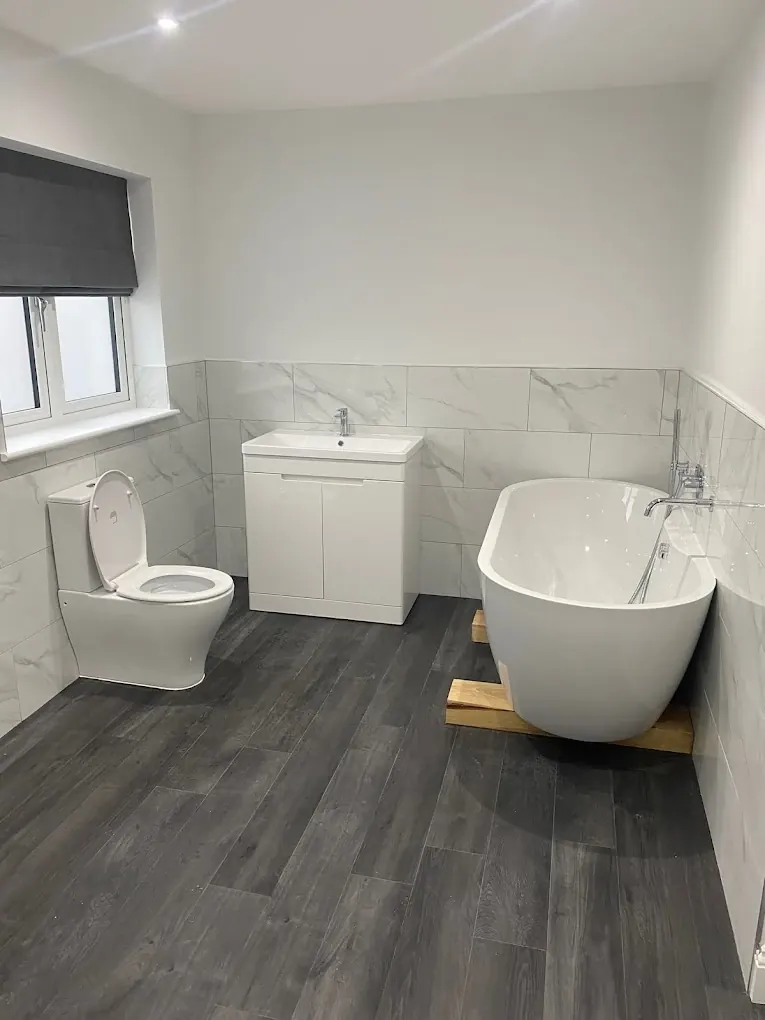 Bright white bathroom with freestanding bath, close-coupled toilet and grey wood-effect floor